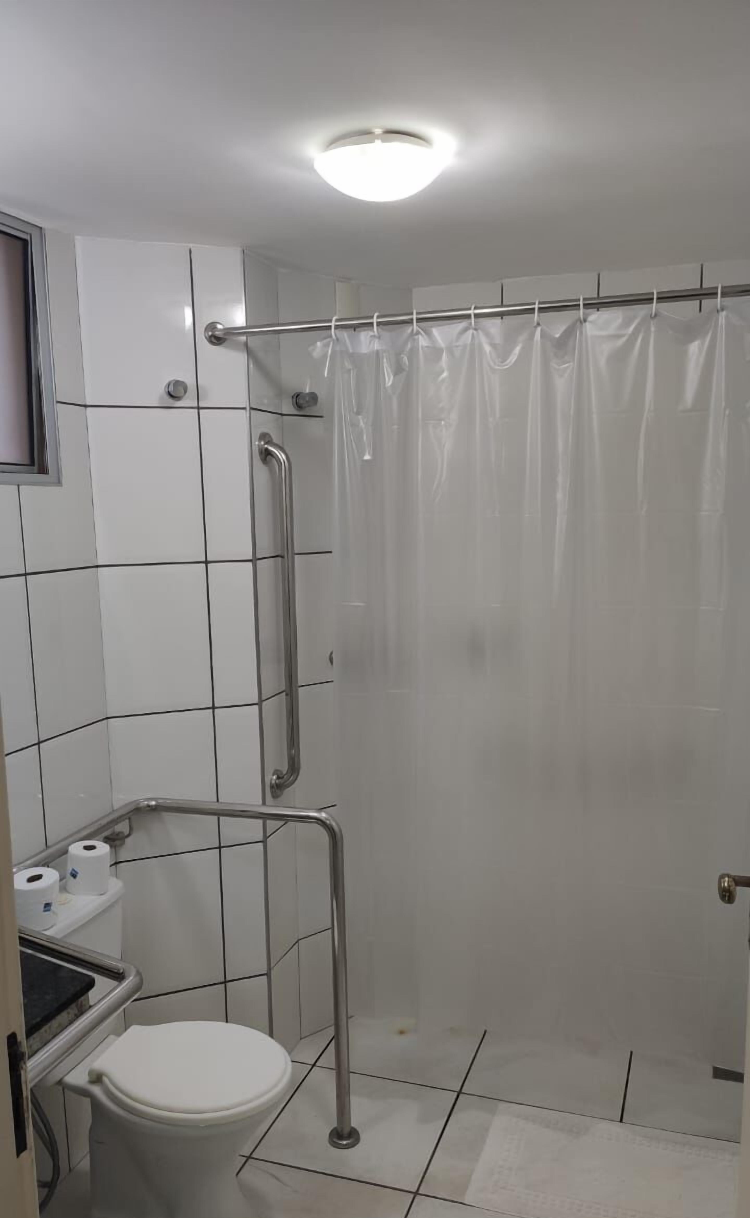 A small, modern bathroom with a toilet, a shower with a glass door, and a handrail.