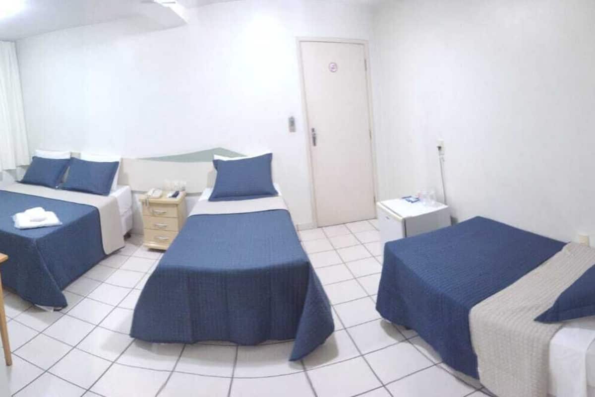 A hotel room with three beds, a bedside table, a small desk, and a wardrobe.