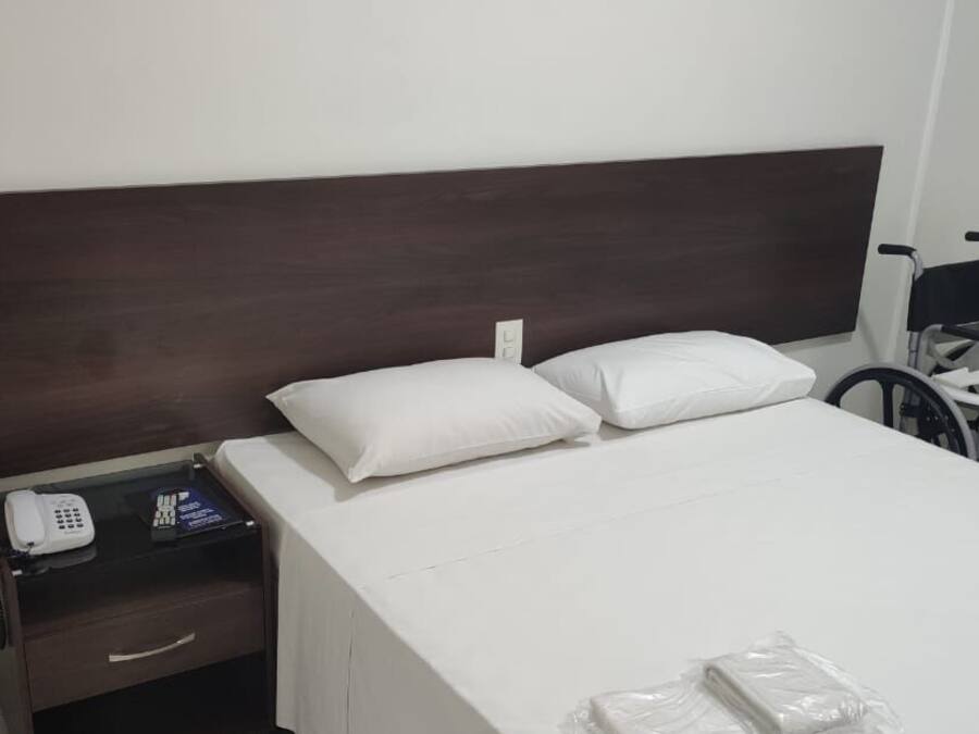 A hotel room with a single bed, a bedside table with a phone, and a wheelchair.