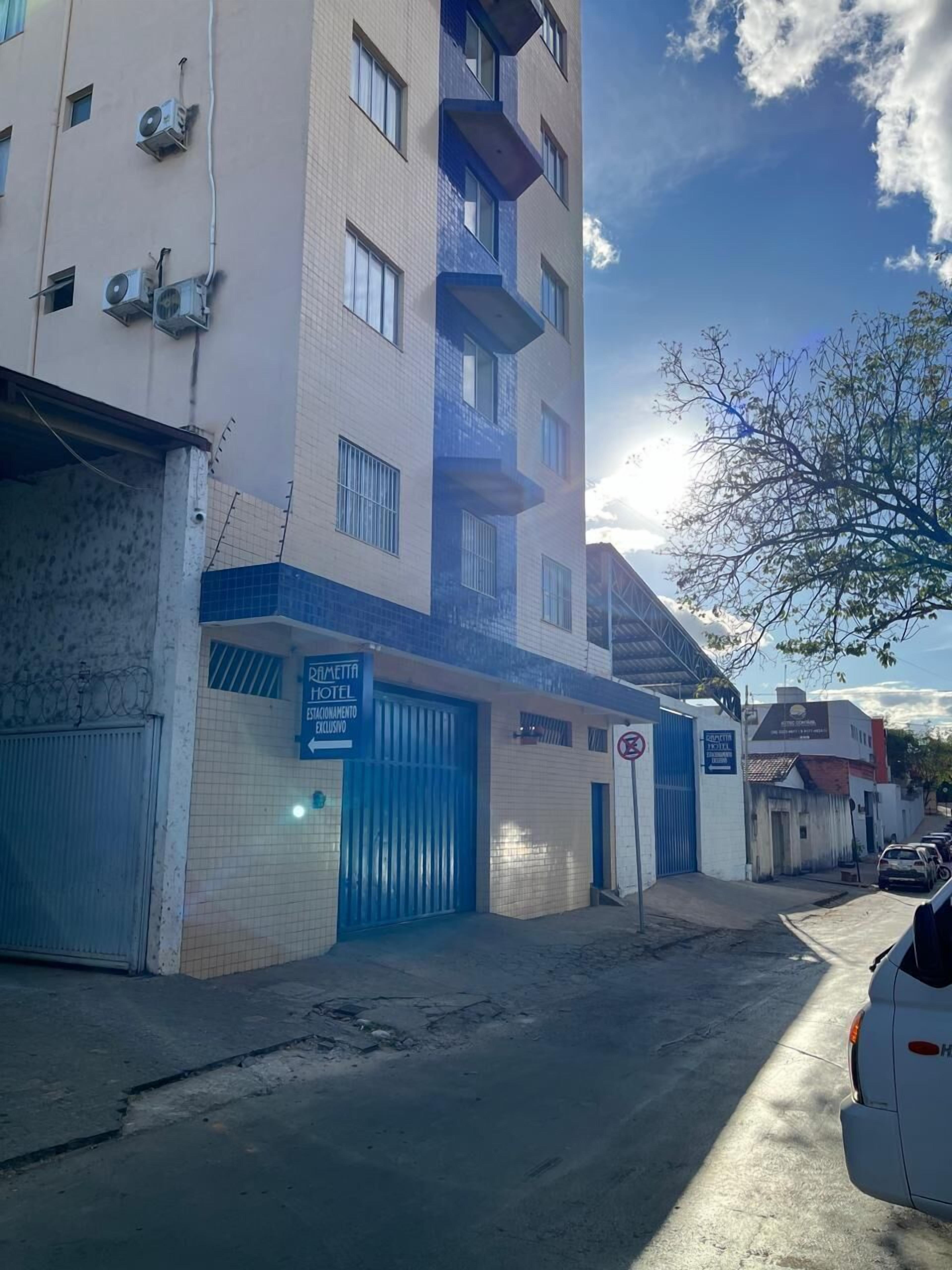 Un hotel con fachada azul y blanca, unidades de aire acondicionado y una entrada protegida por un portón.
