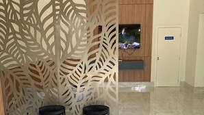A lobby with a reception desk, two black round tables, a decorative leaf-patterned partition, and a marble floor. - Hotel Rametta (Montes Claros)