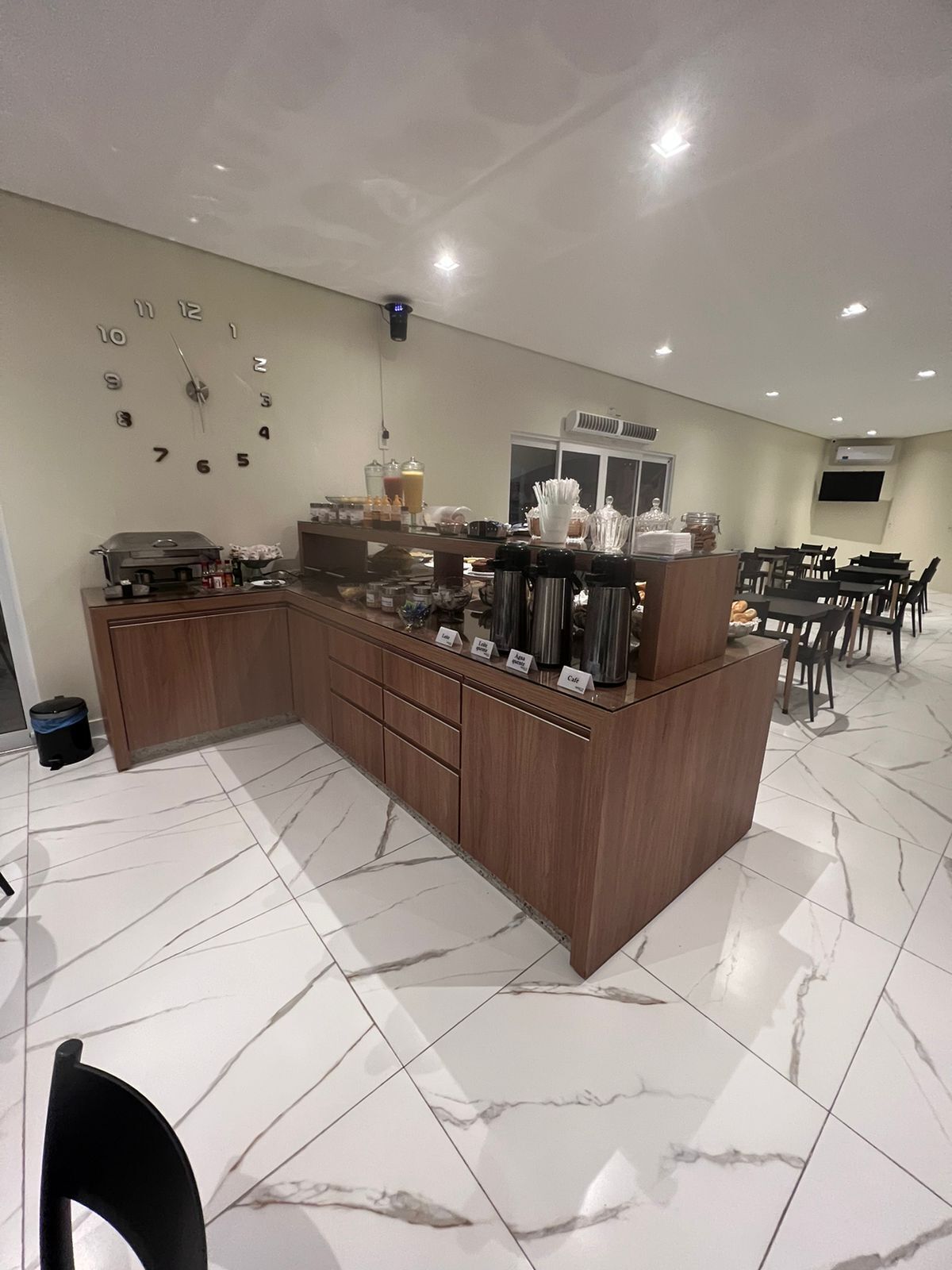 A modern kitchen area with a marble floor, wooden cabinets, and a coffee station with various appliances and containers.