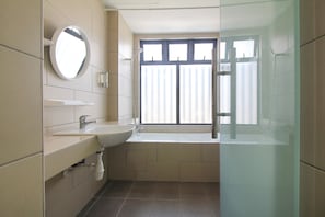 Bathroom features a round mirror, sink, and bathtub with a glass-enclosed shower area.