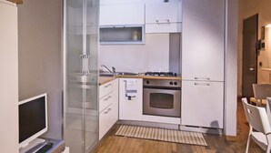 Een compacte keuken met witte kasten, een oven van roestvrij staal, een klein raam en een houten aanrecht.