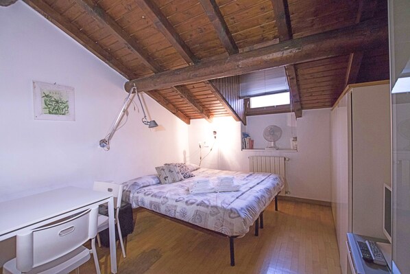 Un dormitorio con techo de madera, una cama con colcha estampada, un escritorio con silla y un radiador.
