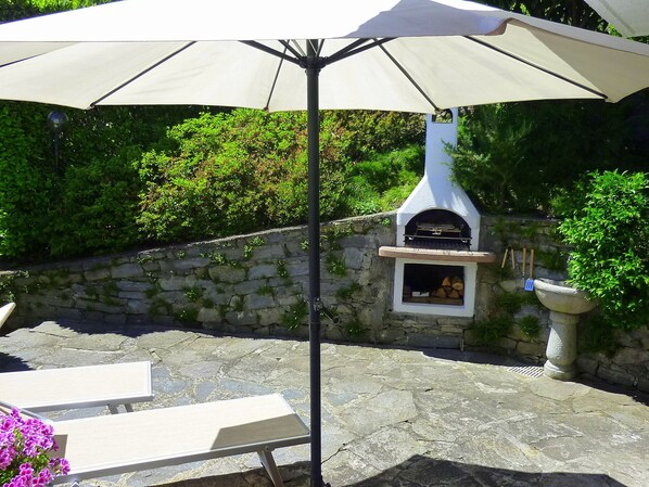 An outdoor patio with stone flooring, a stone wall, a white barbecue grill, and a white umbrella.