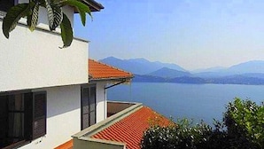 Un edificio moderno de dos pisos con techo de tejas rojas, paredes blancas y vistas a un lago tranquilo y montañas lejanas.