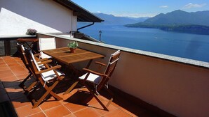 Una terraza con mesa y sillas de madera, una planta en maceta y vistas a un lago y montañas.