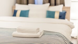 Ein ordentlich bezogenes Bett mit einem gefalteten weißen Handtuch, gestreifter Bettwäsche und zwei Kissen mit blauen und beigen Akzenten.
