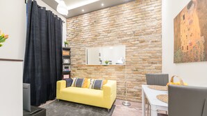 Ein Wohnzimmer mit gelbem Sofa, schwarzem Vorhang, Backsteinwand, großem Spiegel und einem Gemälde.