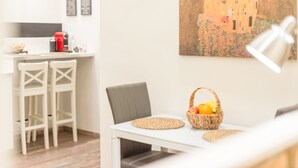 Ein Essbereich mit einem weißen Tisch, zwei Stühlen, einer Obstschale und einem Bild an der Wand.