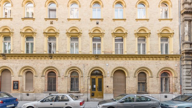 Ein mehrstöckiges Gebäude mit einer symmetrischen Fassade, das Bogenfenster und einen zentralen Eingang aufweist.