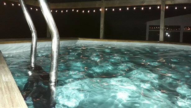 A swimming pool with clear water, metal pool ladders, and string lights in the background. - LE JARRIER DETACHED HOLIDAY RENTAL - ALPES MANCELLES -PRIVATE  POOL -FIBER WIFI (Saint-Georges-le-Gaultier)
