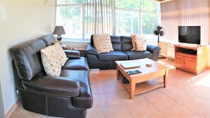 A living room with a sofa, a coffee table, a TV, and a dining area with a table and chairs. - LE JARRIER DETACHED HOLIDAY RENTAL - ALPES MANCELLES -PRIVATE  POOL -FIBER WIFI (Saint-Georges-le-Gaultier)