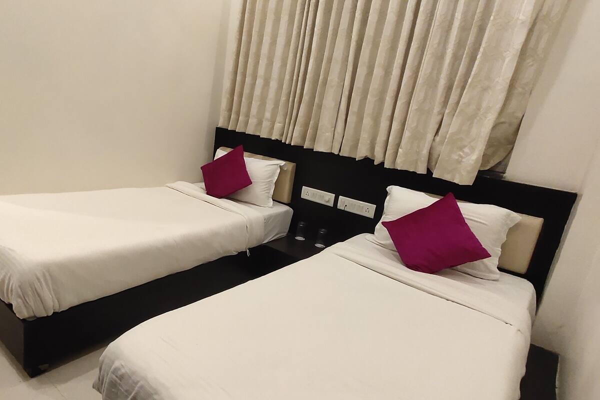 Two single beds with white linens and black headboards, a dark floor, and a white wall with a window covered by curtains.