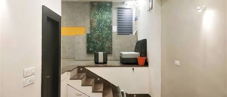 Una escalera moderna con barandilla que conduce a una sala de estar con sofá, una mesita y una planta en maceta.