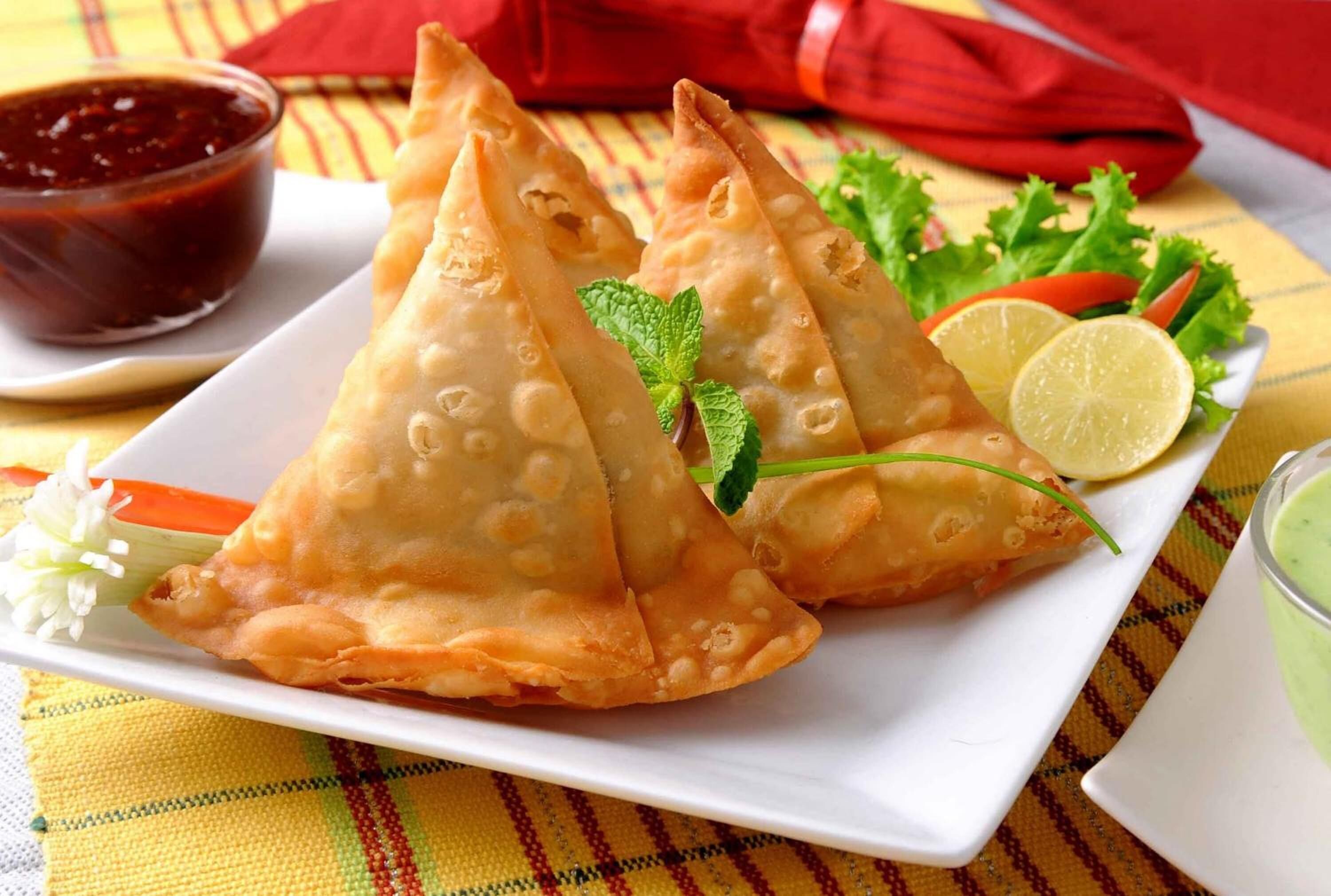 A plate of samosas with a side of chutney and a slice of lime.