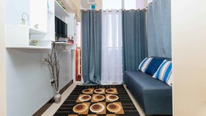 A compact living space with a sofa, a flat-screen TV, a decorative rug, and a small plant. - RedDoorz Plus @ RSG SS Residens Vito Cruz (Manila)