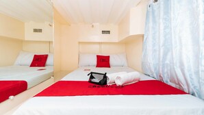 A hotel room with two beds, each with a red and white bedspread, a red pillow, and a small black bag on the bed. - RedDoorz Plus @ RSG SS Residens Vito Cruz (Manila)
