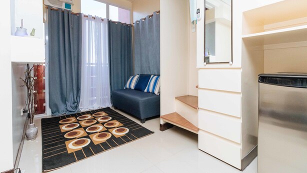 A compact living space with a sofa, a small rug, a mirror, and a staircase. - RedDoorz Plus @ RSG SS Residens Vito Cruz (Manila)