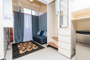 A compact living space with a sofa, a small rug, a mirror, and a staircase. - RedDoorz Plus @ RSG SS Residens Vito Cruz (Manila)