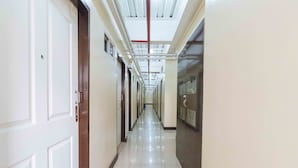 A long, narrow hallway with white doors on one side and a glass wall on the other. - RedDoorz Plus @ RSG SS Residens Vito Cruz (Manila)