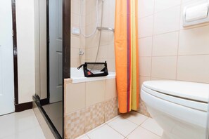 A bathroom with a toilet, a shower, and a shelf with a black basket. - RedDoorz Plus @ RSG SS Residens Vito Cruz (Manila)