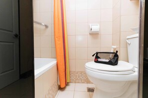 A bathroom with a white toilet, a shower curtain, and a small trash bin on the toilet. - RedDoorz Plus @ RSG SS Residens Vito Cruz (Manila)