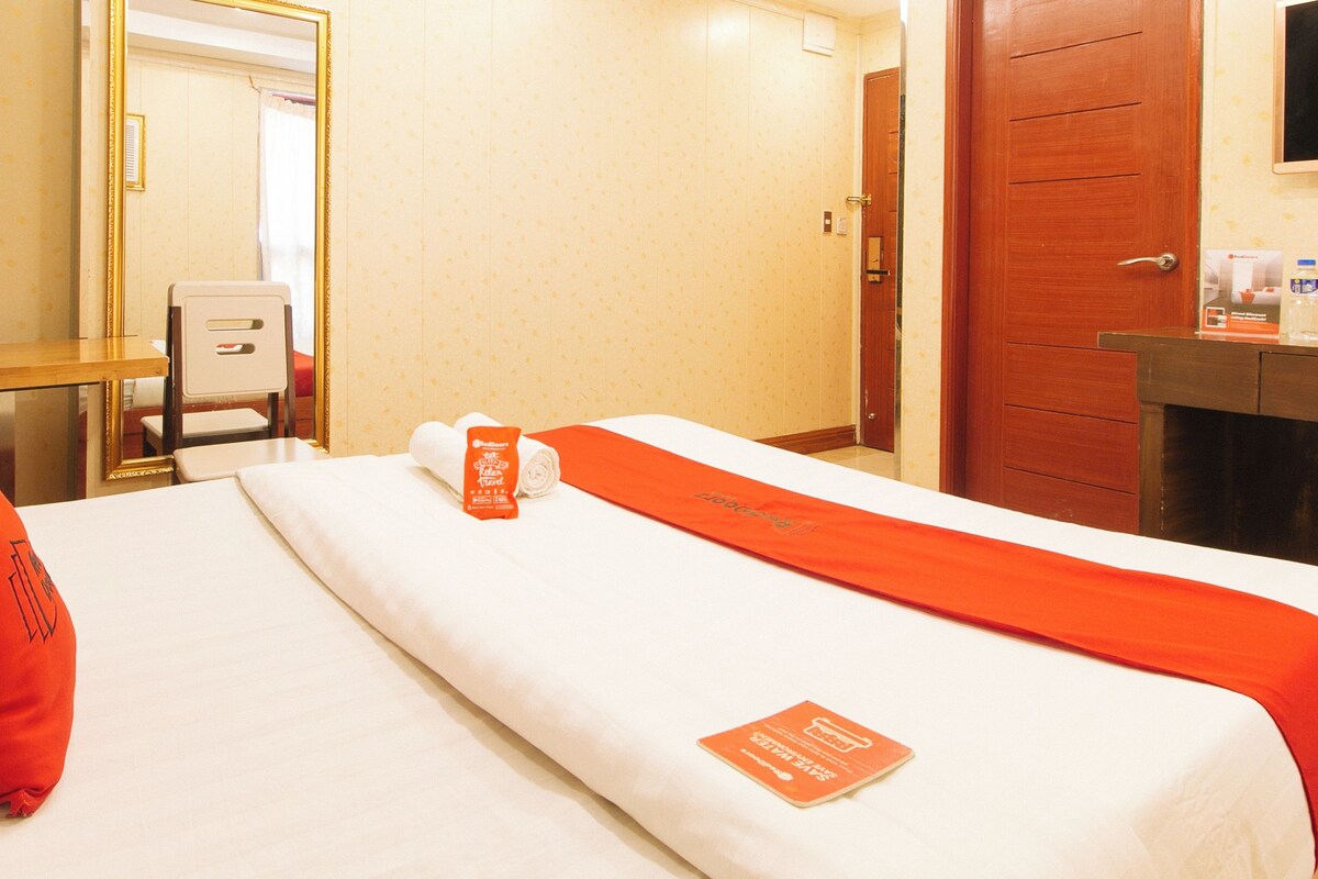 A hotel room with a bed, a desk, a chair, a mirror, and a door.