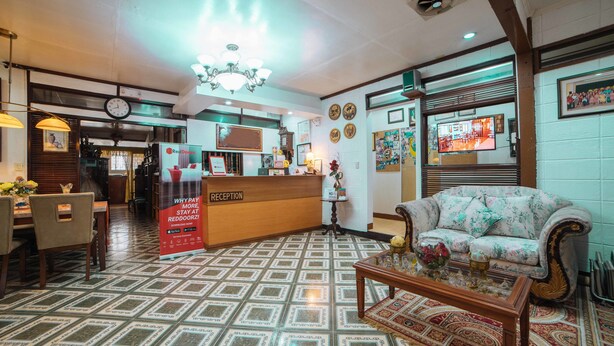A reception area with a reception desk, a clock, a chandelier, a sofa, and a patterned floor. - RedDoorz @ La Casa Guesthouse (Angeles City)