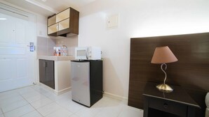 A compact kitchen with a refrigerator, microwave, and a small cabinet. There's a wooden headboard and a lamp on a bedside table. - RedDoorz Premium @ Cityland Tagaytay 2 (Tagaytay)