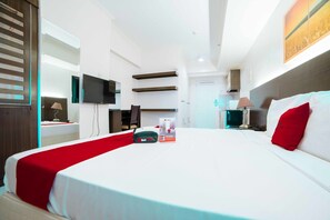 Una habitación de hotel moderna con una cama grande, un televisor de pantalla plana, un escritorio con lámpara y un baño a la vista al fondo.