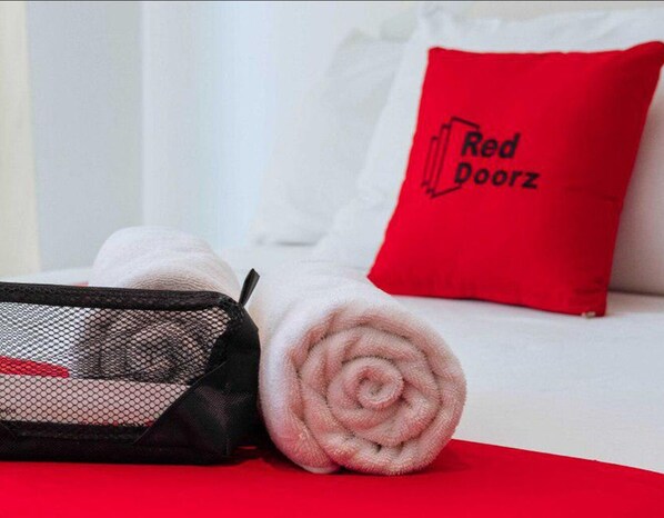 A neatly made bed with a red pillow labeled "Red Doorz" and a rolled towel on the bed. - RedDoorz Premium @ Cityland Tagaytay 2 (Tagaytay)
