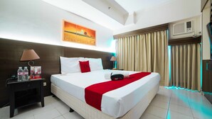 A hotel room with a large bed, a nightstand with a lamp, a painting on the wall, and an air conditioning unit. - RedDoorz Premium @ Cityland Tagaytay 2 (Tagaytay)