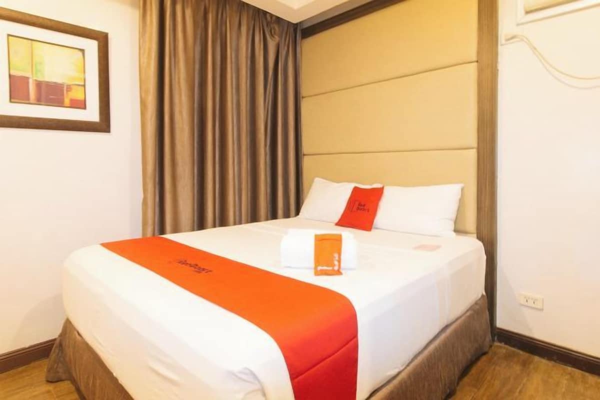 A hotel room with a bed, a framed picture on the wall, and a window with curtains.