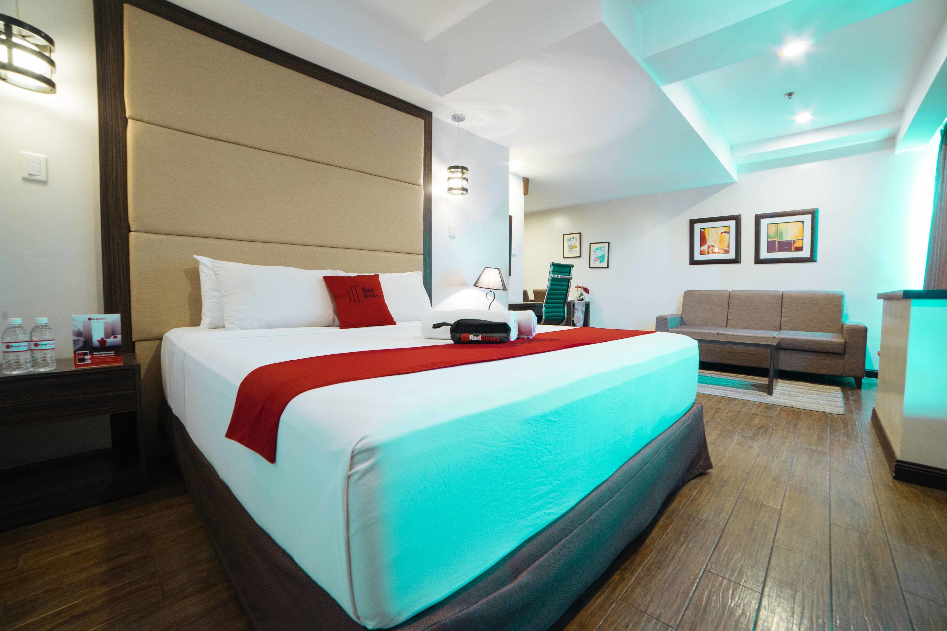 A hotel room with a large bed, a sofa, a desk with a lamp, and a wall-mounted TV.