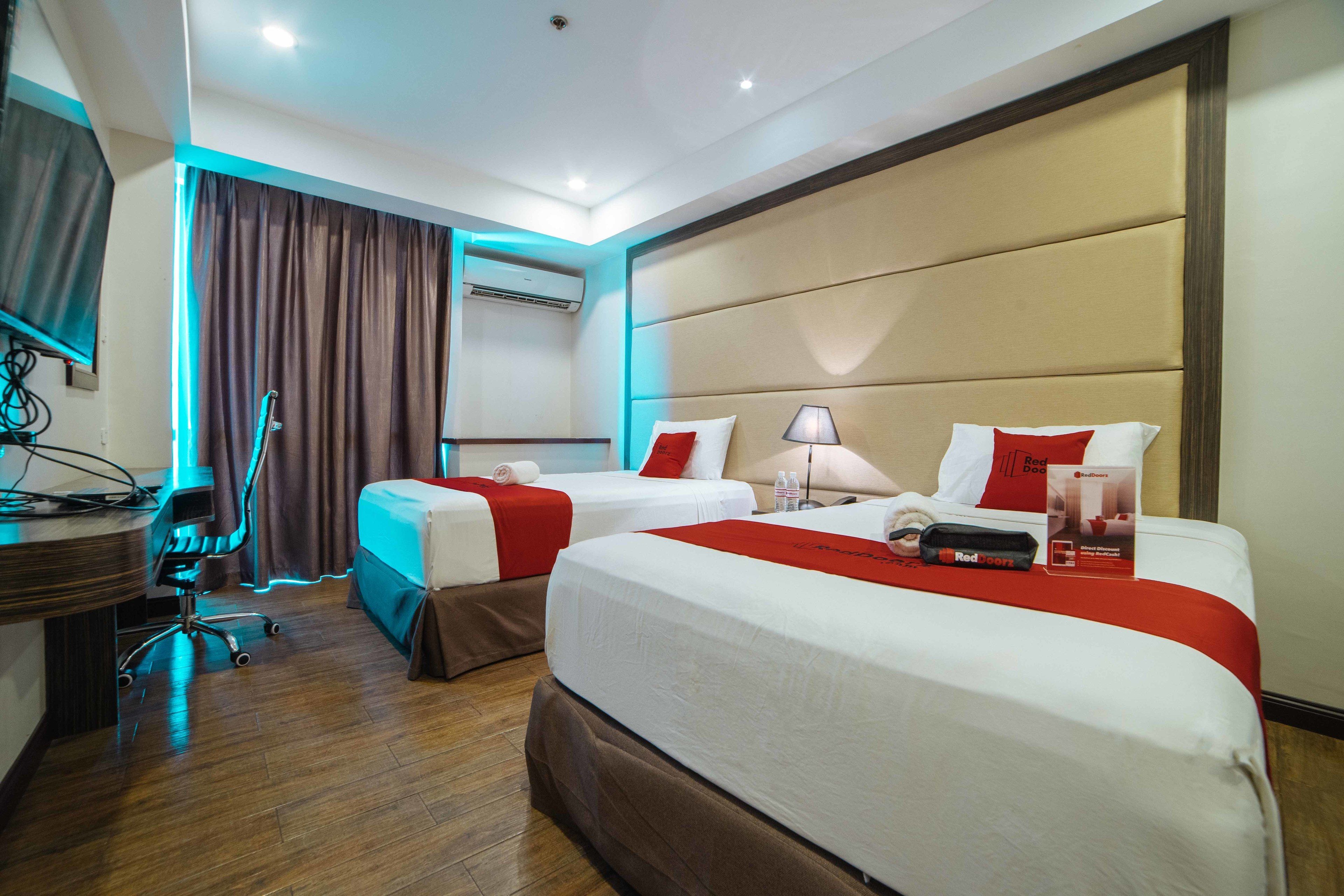 A hotel room with two beds, a desk, a chair, and an air conditioning unit.