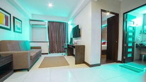 A modern hotel room with a sofa, a desk, a television, and a bathroom visible through an open door. - RedDoorz Premium @ West Avenue Quezon City (Quezon City)