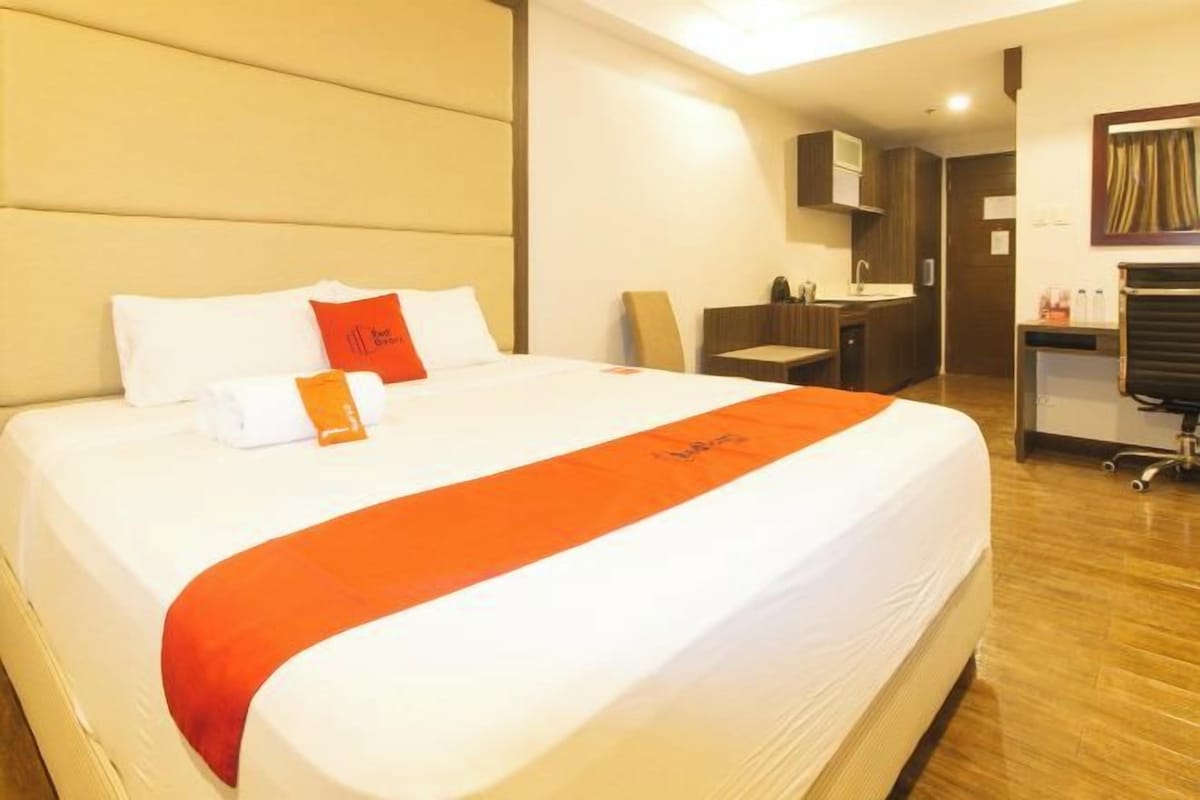 A hotel room with a large bed, a desk, and a kitchenette.