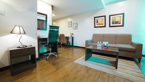 A modern living room with a brown sofa, a coffee table, a desk with a lamp, and a green chair. - RedDoorz Premium @ West Avenue Quezon City (Quezon City)