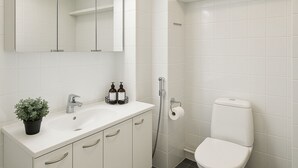 A modern bathroom with white tiles, a sink with a mirror, a toilet, and a shower.