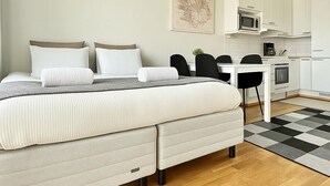A modern bedroom with a bed, bedside tables, a desk, and a kitchenette.