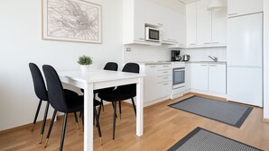 A modern kitchen with white cabinetry, a dining table with black chairs, a microwave, an oven, and a coffee maker.