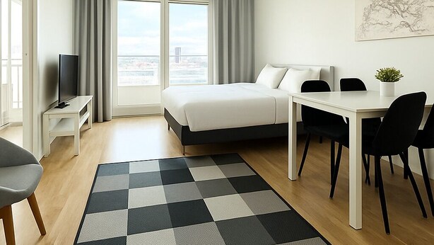 A modern hotel room with a bed, a desk, a chair, a television, and a view of the city through large windows.