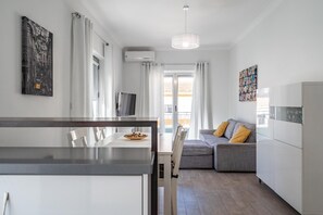 Une cuisine moderne avec un coin repas, un canapé gris agrémenté de coussins jaunes et une grande fenêtre avec des rideaux.
