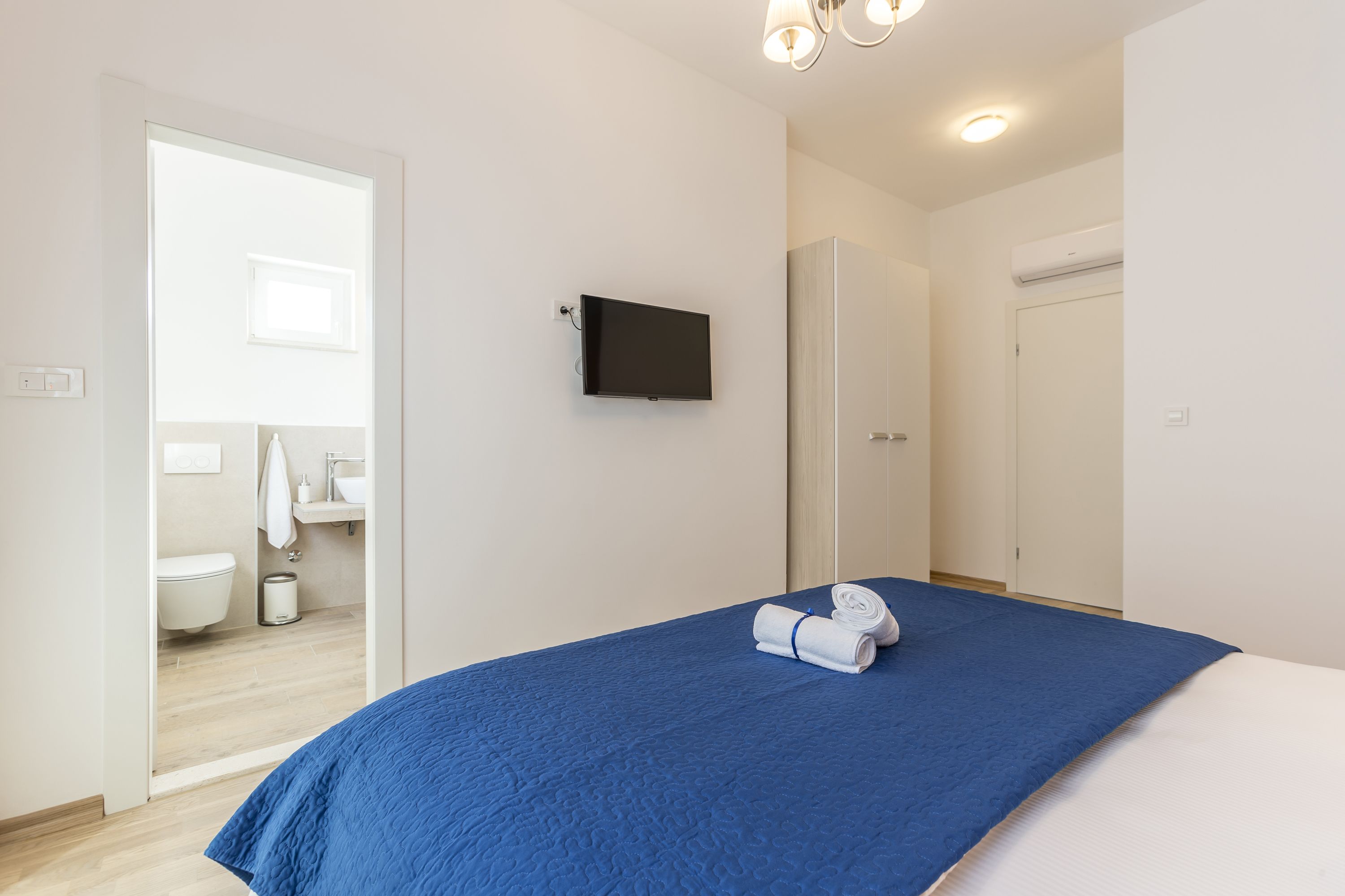 A bedroom with a bed, a television mounted on the wall, and a bathroom visible through an open door.