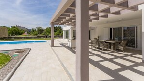 Un patio cubierto con piscina, mobiliario exterior y vistas del barrio circundante.