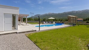 Una casa moderna con piscina, un patio cubierto y vistas a las montañas.