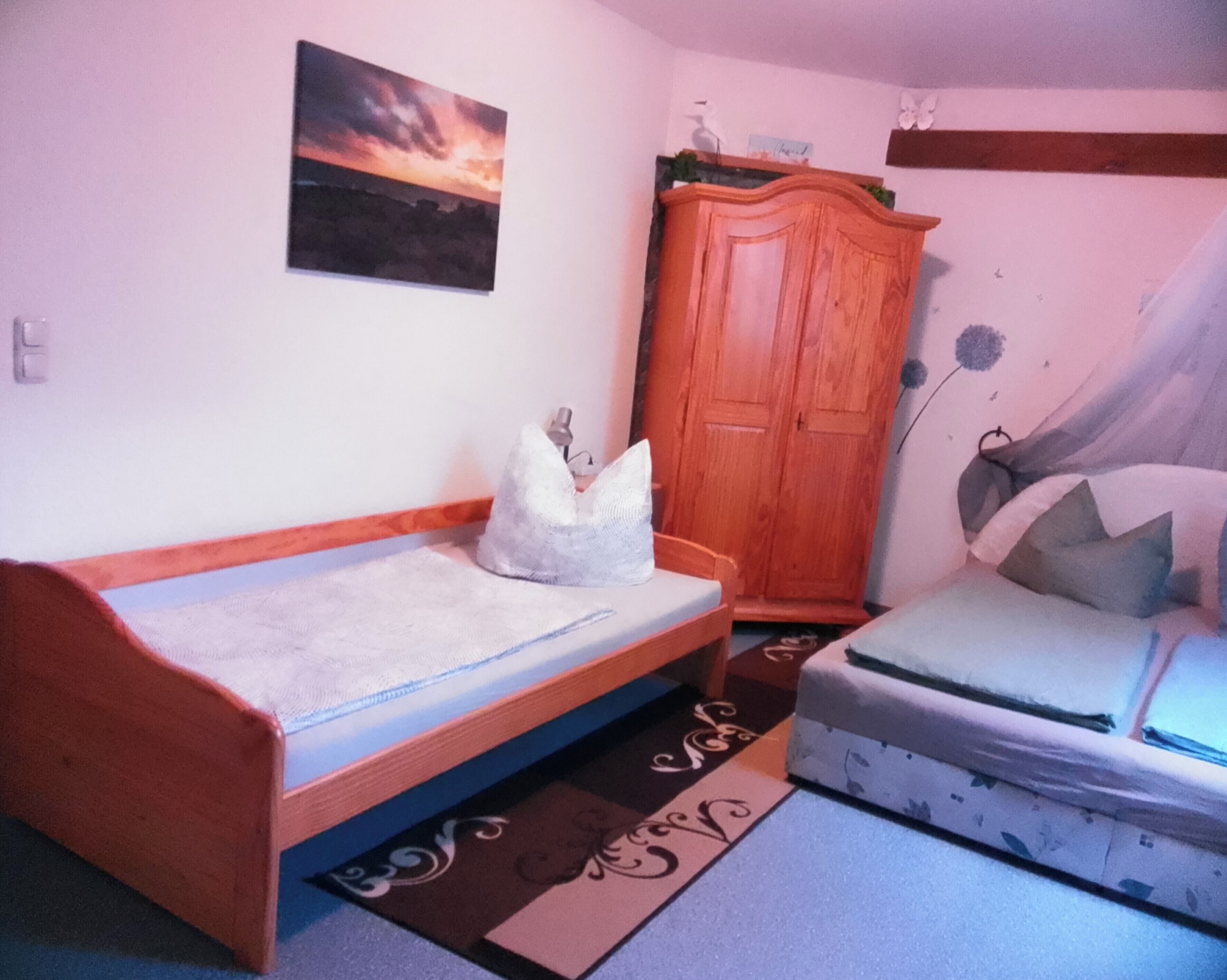 Een slaapkamer met een bed, een houten garderobe en een schilderij aan de muur.