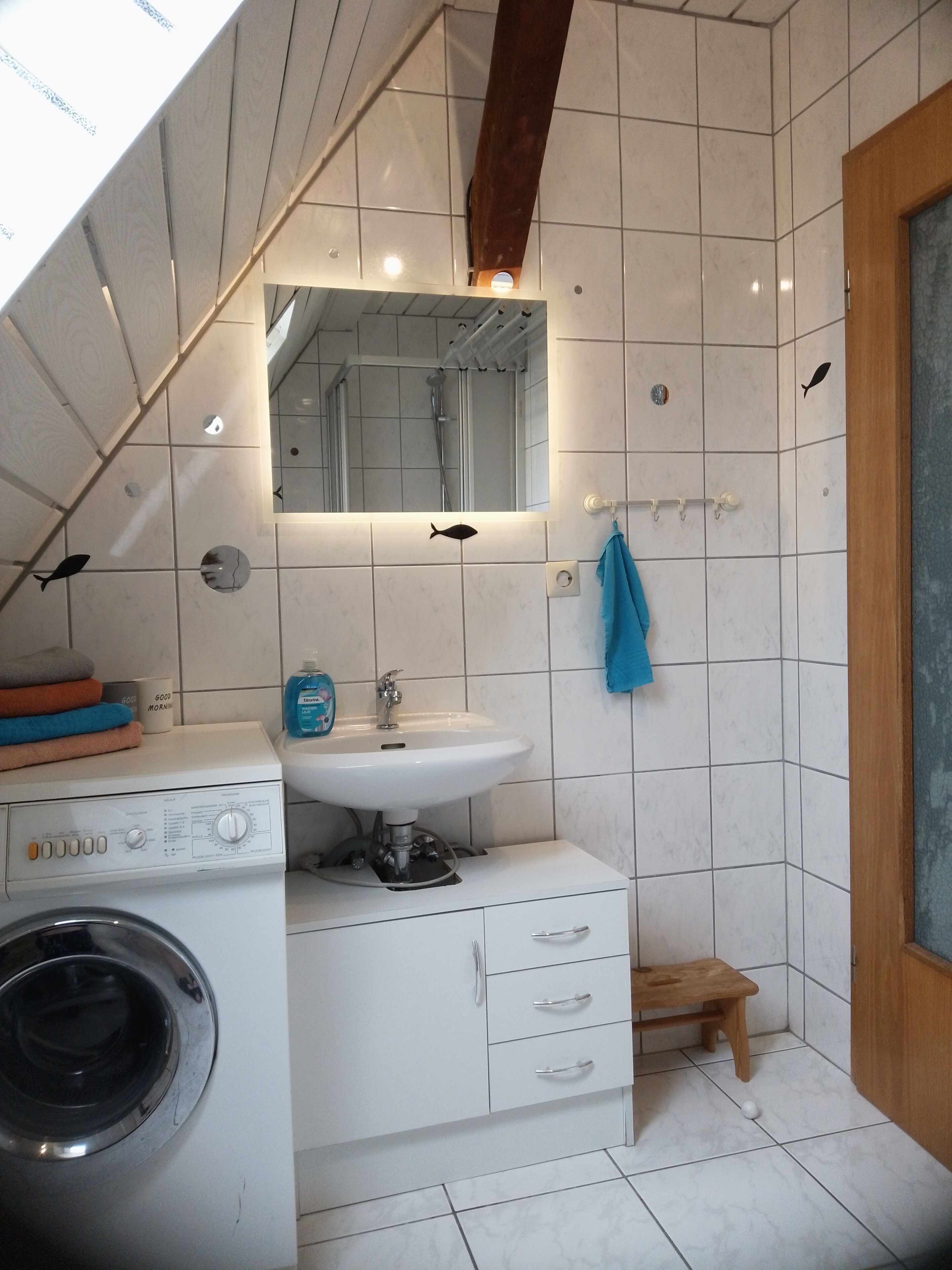 A compact bathroom with a washing machine, a sink, and a shower.